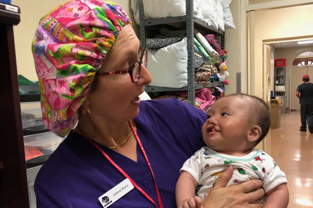 Jolene Bortz in scrubs taking a baby to the surgery room for cleft lip surgery in Antigua, Guatemala.